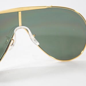 May include: Gold-tone aviator sunglasses with green lenses. The sunglasses have a thin gold frame and a clear plastic nose bridge.
