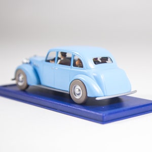 May include: A light blue toy car with four passengers, sitting on a blue display base.