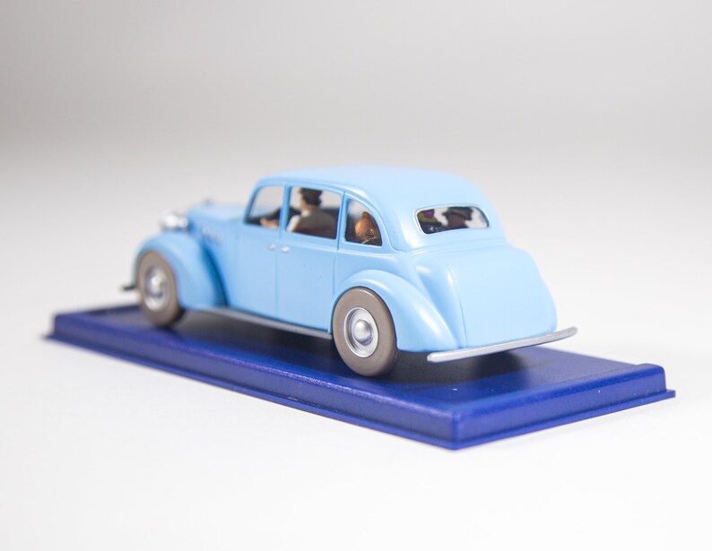 May include: A light blue toy car with four passengers, sitting on a blue display base.