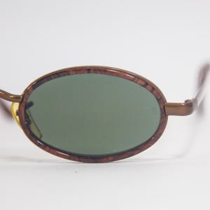 May include: Brown oval sunglasses with green lenses. The frame has a wood grain pattern.