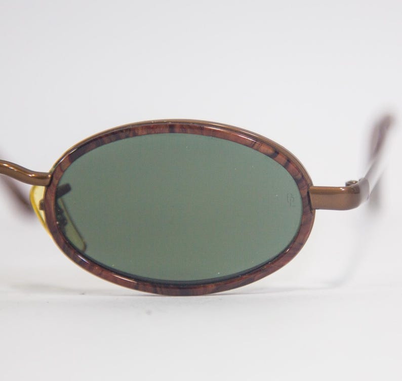 May include: Brown oval sunglasses with green lenses. The frame has a wood grain pattern.
