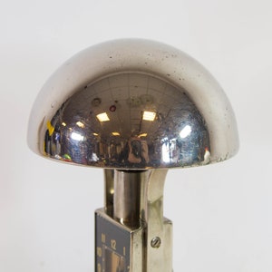 Peut inclure: Une lampe en m&eacute;tal argent&eacute; avec un abat-jour rond et r&eacute;fl&eacute;chissant. L'abat-jour est en forme de d&ocirc;me et a une surface lisse et polie. La lampe a un cadran d'horloge noir avec des chiffres et des aiguilles blancs.