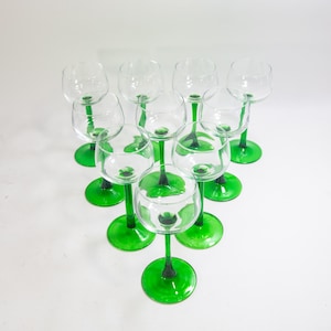 May include: Set of ten clear glass wine glasses with green stems and bases. The glasses are arranged in a circle, with the stems pointing outwards.