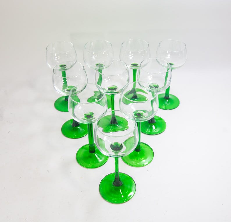 May include: Set of ten clear glass wine glasses with green stems and bases. The glasses are arranged in a circle, with the stems pointing outwards.