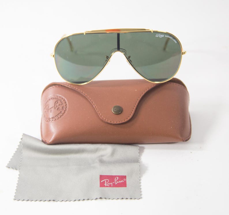 May include: Gold-framed aviator sunglasses with green lenses and a brown leather case. The case has a Ray-Ban logo embossed on the front.