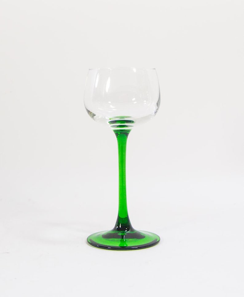 May include: A clear glass wine glass with a green stem and base. The glass has a rounded bowl and a wide base.