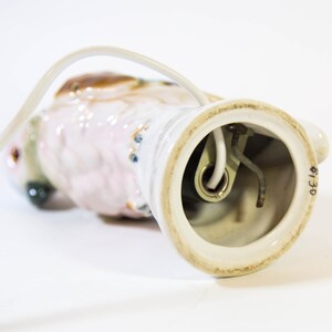 May include: A white ceramic lamp base shaped like a parrot with pink and brown accents. The lamp base has a white cord and a light socket with the number 6130 printed on the bottom.