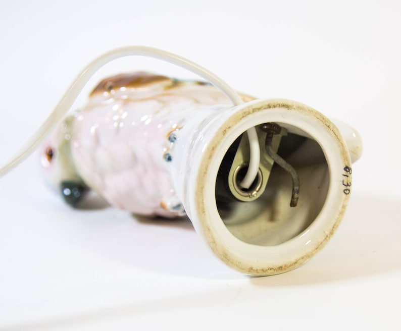 May include: A white ceramic lamp base shaped like a parrot with pink and brown accents. The lamp base has a white cord and a light socket with the number 6130 printed on the bottom.