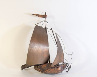 May include: A copper sailboat sculpture with a single sail and a small flag. The sailboat is made of thin copper sheets and wire.