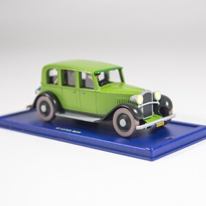 May include: A green toy car model with a blue base. The car has a black grill and headlights, and a license plate that reads "2314".