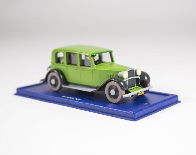 May include: A green toy car model with a blue base. The car has a black grill and headlights, and a license plate that reads "2314".