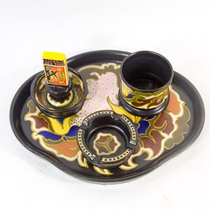 May include: A vintage black ceramic smoking set with a tray, ashtray, match holder, and cup. The tray and pieces feature a floral design in yellow, brown, blue, and pink. A matchbox with the word "ZARIN" is visible.