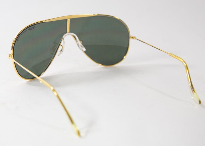 May include: Gold aviator sunglasses with green lenses. The sunglasses have a thin gold frame and a gold nose bridge.