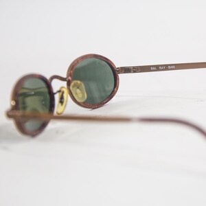 May include: Brown tortoise shell frame sunglasses with green lenses. The sunglasses have a metal bridge and arms. The brand name "B&L RAY-BAN" is printed on the right arm.