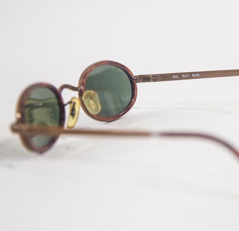 May include: Brown tortoise shell frame sunglasses with green lenses. The sunglasses have a metal bridge and arms. The brand name "B&L RAY-BAN" is printed on the right arm.