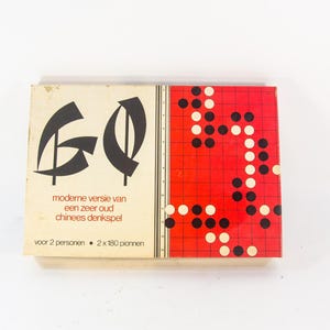 May include: A vintage game box with the word "GO" in black lettering on a white background. The box features a red and white game board with black and white playing pieces. The text on the box reads "moderne versie van een zeer oud chinees denkspeel voor 2 personen - 2 x 180 pionnen".