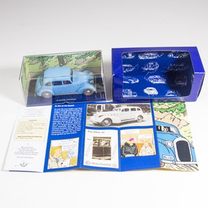 May include: A blue toy car in a clear plastic box with a blue and white cardboard box. The box has a picture of the car and the text "Le Voltigeur", "De auto van het Suskewiet", and "From albums 1953".