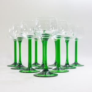 May include: A set of nine clear glass wine glasses with green stems. The glasses are arranged in a row on a white surface.