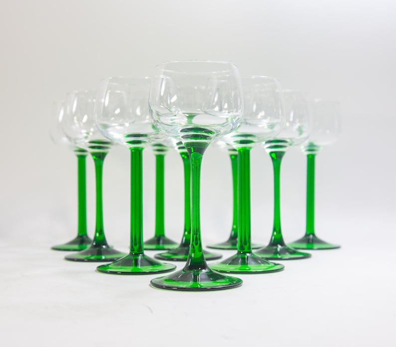 May include: A set of nine clear glass wine glasses with green stems. The glasses are arranged in a row on a white surface.