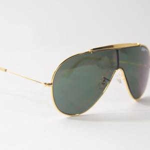 May include: Gold-framed aviator sunglasses with green lenses. The sunglasses have a distinctive, wraparound design.