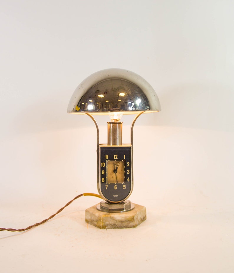 Peut inclure: Une lampe de table argent&eacute;e et noire avec un abat-jour en forme de d&ocirc;me et un cadran d'horloge. Le cadran de l'horloge a des chiffres romains noirs et un fond blanc. La lampe est sur une base en marbre blanc.