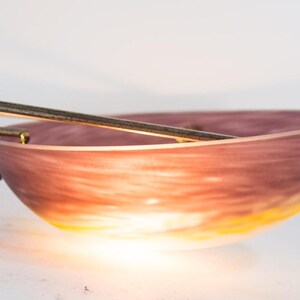Pu&ograve; includere: Una ciotola decorativa con una sfumatura di colori, che passa da un viola intenso a un giallo caldo. La ciotola ha un aspetto liscio e traslucido ed &egrave; impreziosita da dettagli metallici argentati. Due aste metalliche sono poste sopra la ciotola.