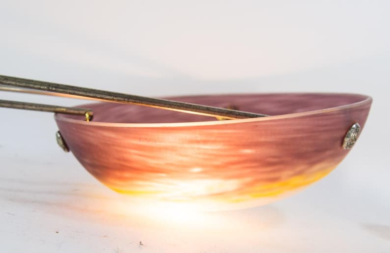 Pu&ograve; includere: Una ciotola decorativa con una sfumatura di colori, che passa da un viola intenso a un giallo caldo. La ciotola ha un aspetto liscio e traslucido ed &egrave; impreziosita da dettagli metallici argentati. Due aste metalliche sono poste sopra la ciotola.