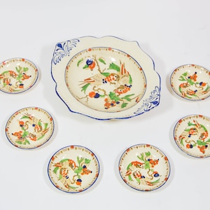 May include: A set of six vintage ceramic plates with a white background and a blue and gold border. The plates feature a colourful design of birds and flowers.