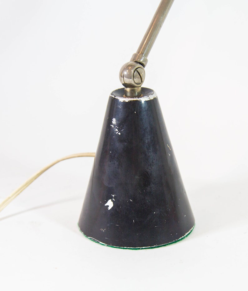 Może przedstawiać: Czarna metalowa lampa biurkowa z kloszem w kształcie stożka i regulowanym srebrnym ramieniem. Lampa ma zieloną filcową podstawę.