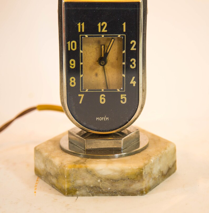 Peut inclure: Un r&eacute;veil vintage argent&eacute; et noir avec une base en marbre. Le cadran de l'horloge a des chiffres et des aiguilles dor&eacute;s. L'horloge est fabriqu&eacute;e par la soci&eacute;t&eacute; "Mof&eacute;m".