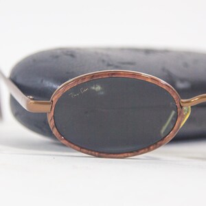 May include: Brown oval-shaped sunglasses with dark lenses and a Ray-Ban logo on the frame.