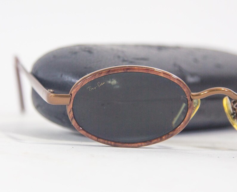 May include: Brown oval-shaped sunglasses with dark lenses and a Ray-Ban logo on the frame.