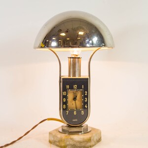 Peut inclure: Une lampe de table argent&eacute;e et noire avec un abat-jour en d&ocirc;me chrom&eacute; et un cadran d'horloge avec des chiffres romains. La lampe est sur un socle en marbre et a un cordon.