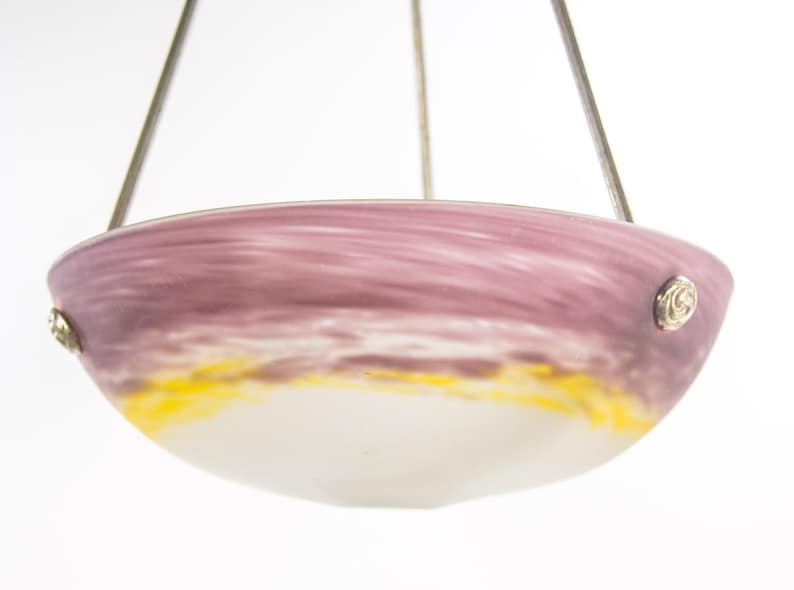 Pu&ograve; includere: Un lampadario in vetro con un paralume a forma di ciotola. Il paralume presenta una miscela di colori, tra cui viola, giallo e bianco. Il lampadario &egrave; sospeso da sottili fili metallici e presenta accenti metallici decorativi.