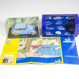 May include: A blue toy car in a clear plastic box with a comic book style illustration of the car on the box. The car is also pictured in a comic book style illustration on a yellow and blue folded card with the text "De Scepter Van Ottokar" on the card.