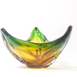 Könnte beinhalten: Eine grüne und bernsteinfarbene Glasschale mit einer einzigartigen, organischen Form. Die Schale ist aus mundgeblasenem Glas gefertigt und hat eine glänzende Oberfläche.