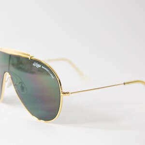 May include: Gold aviator sunglasses with green lenses and the text "Wayfarer Bausch & Lomb" on the frame.