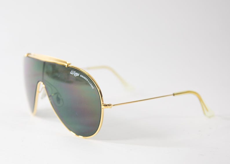 May include: Gold aviator sunglasses with green lenses and the text "Wayfarer Bausch & Lomb" on the frame.