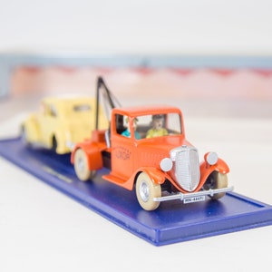 Puede incluir: Un cami&oacute;n de remolque rojo de juguete con un coche amarillo en remolque. El cami&oacute;n de remolque tiene un conductor y un pasajero en la cabina. El cami&oacute;n de remolque tiene la palabra "Luxor" impresa en el lateral. La matr&iacute;cula dice "MN-64471".
