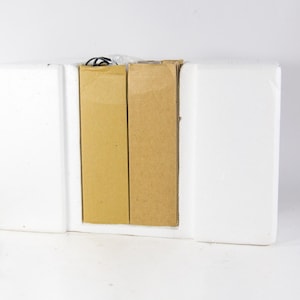 May include: Two brown cardboard boxes are inside a white polystyrene box. The boxes are sealed and have no visible markings.