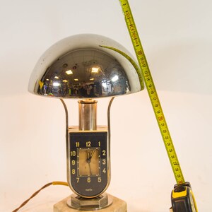 Peut inclure: Une lampe de table en chrome et en marbre avec un cadran d'horloge qui indique "maren". La lampe a un abat-jour en forme de d&ocirc;me et une base argent&eacute;e.