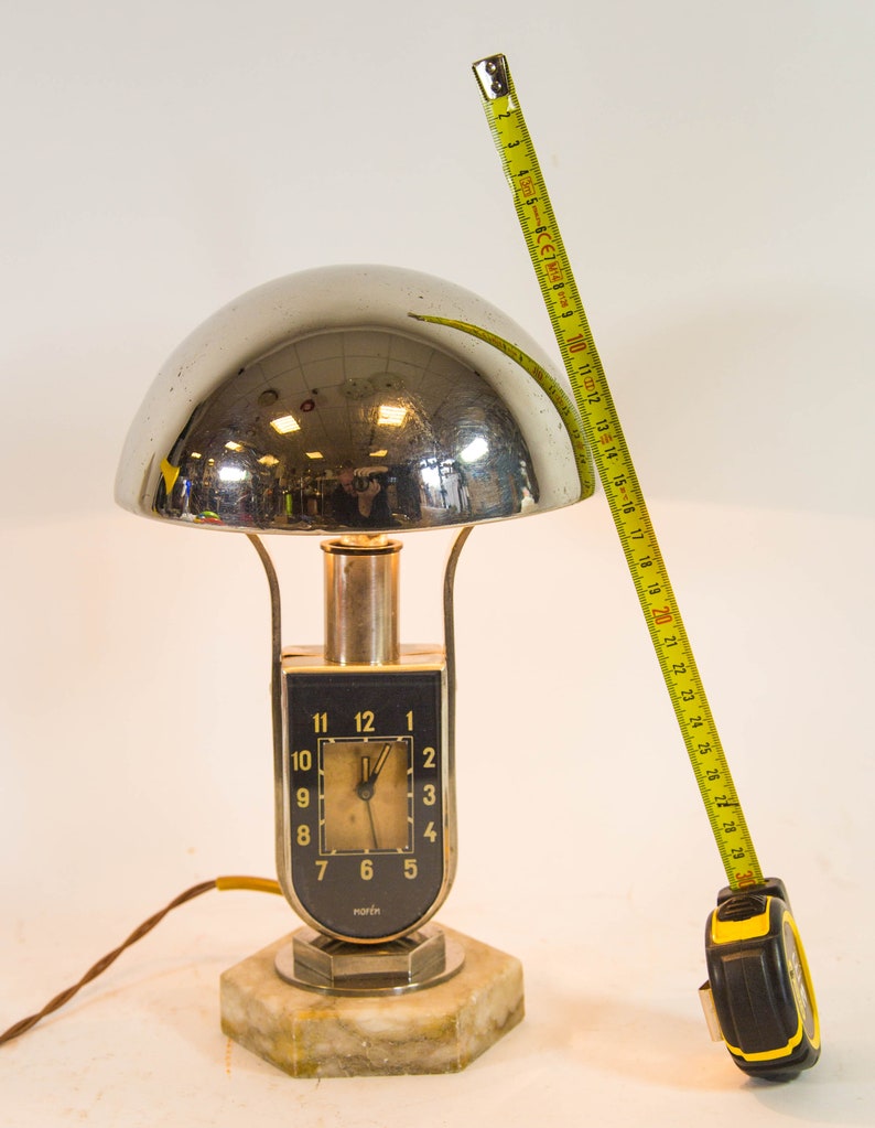 Peut inclure: Une lampe de table en chrome et en marbre avec un cadran d'horloge qui indique "maren". La lampe a un abat-jour en forme de d&ocirc;me et une base argent&eacute;e.