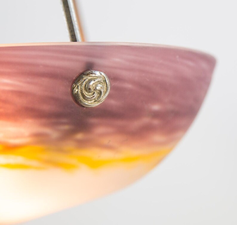 Pu&ograve; includere: Primo piano di un paralume decorativo in vetro con una sfumatura di colore, che passa dal viola scuro in alto al giallo vibrante in basso. Un bottone argentato ornato &egrave; fissato sul lato.