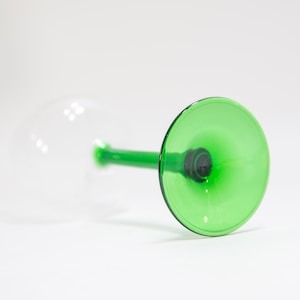 May include: A green glass wine glass with a clear stem and base. The glass is upside down, showing the green interior.