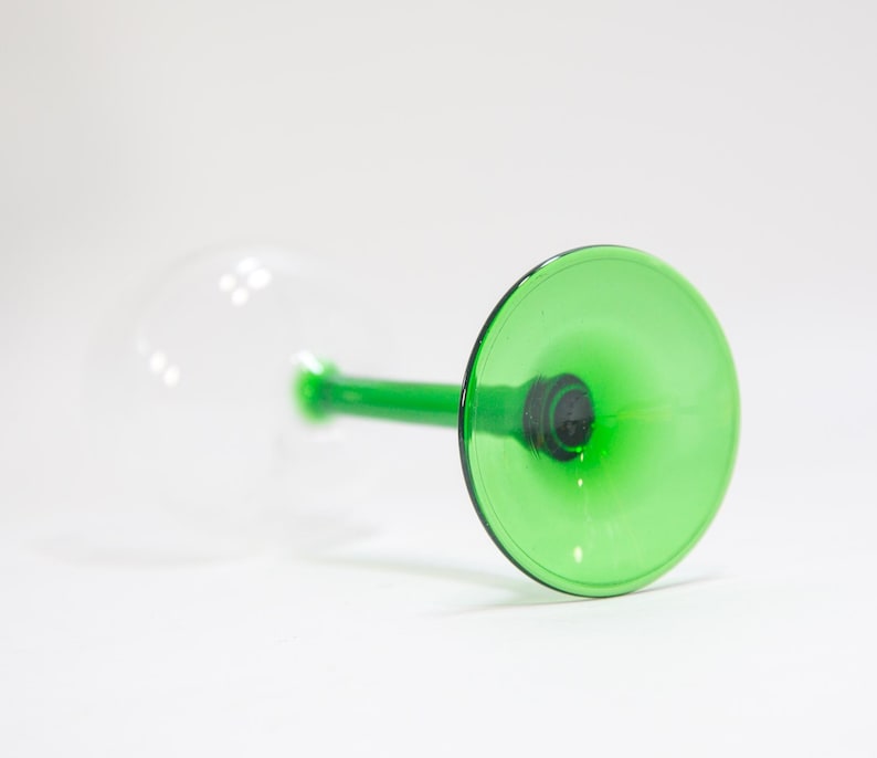 May include: A green glass wine glass with a clear stem and base. The glass is upside down, showing the green interior.