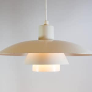 May include: A white pendant light with a layered, saucer-shaped design. The light is suspended from a white cord.