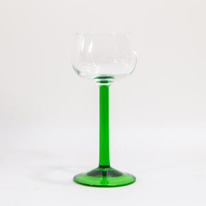 May include: A tall, clear glass with a green stem and base. The glass is designed for drinking wine or other beverages.