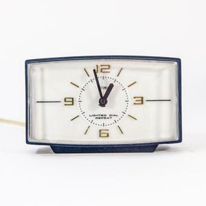 May include: A white analogue clock with black hands and gold numbers. The clock has a black plastic case and a white face with the text "Lighted Dial Repeat".