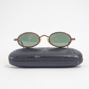 May include: A pair of brown oval-shaped sunglasses with green lenses and a black case.