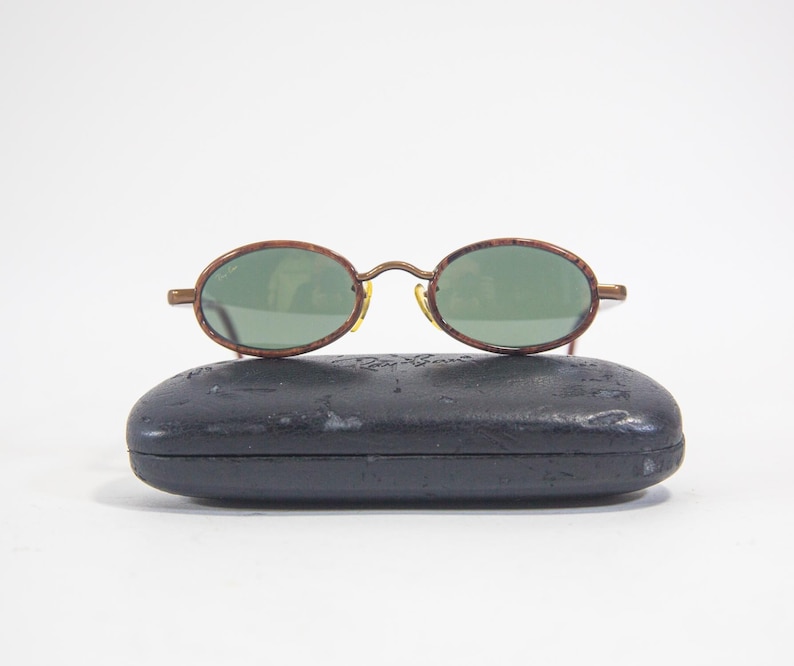 May include: A pair of brown oval-shaped sunglasses with green lenses and a black case.